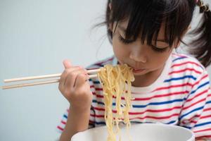 Cute Asian child girl eating delicious instant noodles at home. photo