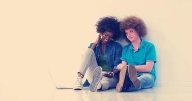 pareja multiétnica sentada en el suelo usando una computadora portátil y una tableta foto