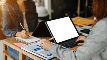 People using and looking at mockup laptop computer on wooden table together on office desk with clipping path tablet photo
