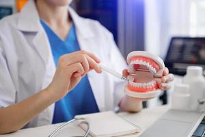 dentista sentado a la mesa con muestras de mandíbula modelo de diente y trabajando con tableta y computadora portátil en el consultorio dental clínica dental profesional. medico trabajando foto