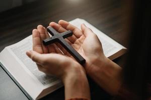 Woman sitting and studying the scriptures.The  wooden cross in the hands. Christian education concepts The Holy Scriptures open and pray to God. photo