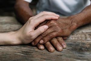 Hands of the old man and a woman hand on the wood table in sun light photo