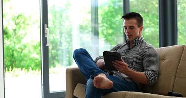 Man is Laying on Couch at Home and Using Tablet photo