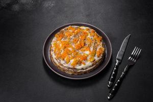 Delicious fresh liver cake with mayonnaise and carrots on a black plate against a dark concrete background photo