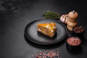 Delicious fresh liver cake with mayonnaise and carrots on a black plate against a dark concrete background photo