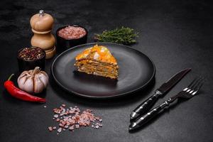 Delicious fresh liver cake with mayonnaise and carrots on a black plate against a dark concrete background photo