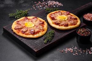 Homemade pizza with sausages, tomatoes, cheese, spices and herbs on a wooden cutting board photo