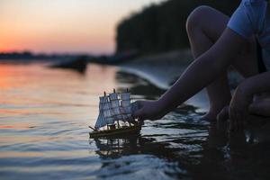 A boy launches a toy decorative ship at sunset. Children's outdoor recreation in summer. photo
