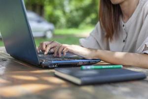 Hands pressed on the laptop keyboard on the desk outdoors in the shady atmosphere suitable for working. photo