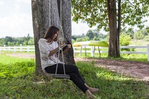 Beautiful Asian woman sitting on a swing and writing something down in a notebook. photo
