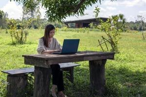 un agricultor moderno dirige un negocio en línea con una computadora portátil en una mesa de madera en el huerto. foto