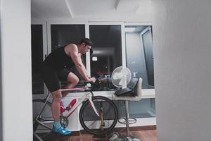 Man cycling on the machine trainer he is exercising in the home at night playing online bike racing game photo