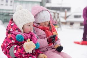 portrait of two little grils sitting together on sledges photo