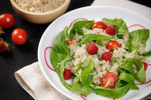 Quinoa salad with vegetables, raspberry and tomatoes on the black table. Super food for healthy and concept of balanced diet photo