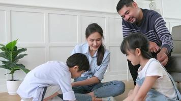 asiatische thailändische geschwister und mutter sitzen auf dem boden des wohnzimmers, zeichnen zusammen mit buntstiften, vater entspannt sich gemütlich auf einem sofa, schöne fröhliche wochenendaktivität und häuslicher wohlbefindenslebensstil. video