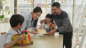 feliz familia asiática tailandesa, niños pequeños sorprendidos por pastel de cumpleaños, regalo, soplar una vela y celebrar la fiesta con padres y hermanos juntos en la mesa del comedor, evento especial de bienestar doméstico en el hogar.