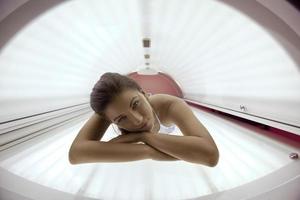 Beautiful young woman tanning in solarium photo