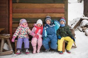 grupo de niños pequeños sentados juntos frente a una cabaña de madera foto