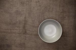 Cuenco redondo de cerámica blanca en blanco vacío sobre fondo negro de mesa de madera con espacio para copiar, vista superior del concepto tradicional de utensilios de cocina hechos a mano foto