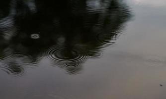 la lluvia cae sobre la superficie del estanque con el reflejo del cielo azul como si se sintiera triste o solo. foto