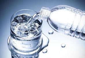 Pouring fresh pure water from bottle into a glass on the table with water drops, Healthcare and beauty hydration concept photo