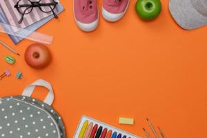 Top view mockup of Education's accessories with backpack, student books, shoes, colorful crayon, eye glasses, empty space isolated on orange background, Concept of education and back to school photo