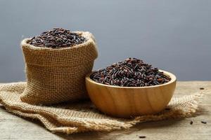 Rice berry or uncooked brown rice in bowl and burlap sack on wooden table photo
