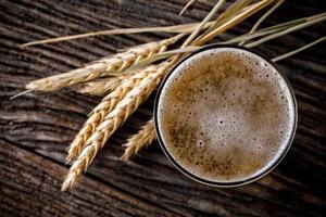 Glasses of light beer with barley on wooden table. Two glass of beer with wheat on wooden table. Vintage style color effect photo