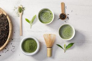 polvo de té verde matcha orgánico en un tazón con batidor de alambre y hoja de té verde sobre una mesa de piedra blanca, producto orgánico de la naturaleza para la salud con estilo tradicional foto