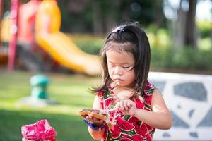 retrato de un niño de 4-5 años. linda chica asiática está untando chocolate en una rebanada de pan, mientras se relaja en el parque. durante el verano o la primavera. los niños tienen hambre. espacio vacío para ingresar texto. foto