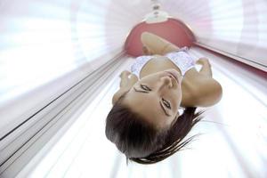 Beautiful young woman tanning in solarium photo