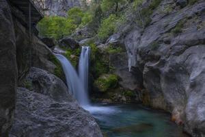 Mountain waterfall in a rocky gorge overgrown with green forest. Stream of icy water falls on mossy stones. photo