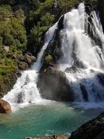 cascada de montaña en un desfiladero rocoso cubierto de bosque verde. corriente de agua helada cae sobre piedras cubiertas de musgo. foto