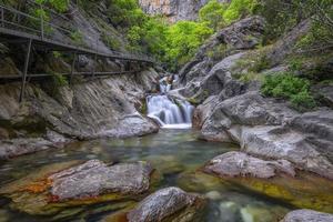 Mountain waterfall in a rocky gorge overgrown with green forest. Stream of icy water falls on mossy stones. photo