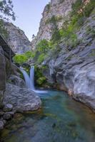 Mountain waterfall in a rocky gorge overgrown with green forest. Stream of icy water falls on mossy stones. photo