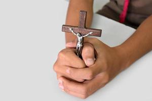 Wooden cross with a statue of Jesus crucified by his arm holding in hands of prayer on white table in the churce, soft and selective focus.