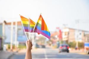banderas del arco iris sosteniendo en la mano al lado del símbolo lgbtq de la carretera rural, concepto para llamar y mostrar a los pasajeros y conductores que apoyen y respeten a las personas lgbtq en el mes del orgullo en todo el mundo. foto