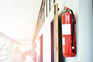 un extintor de incendios rojo está instalado en una pared de cemento blanco en el porche delantero del edificio para ser utilizado para extinguir un incendio en caso de incendio en un edificio. foto