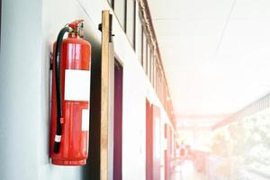 A red fire extinguisher is installed on a white cement wall in the front porch of the building to be used to extinguish a fire in the event of a building fire. photo