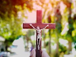 A black wooden cross with a statue of Jesus crucified by his arm. Behind it is the walk way of a school in an Asian country, soft and selective focus. photo