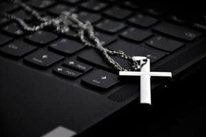 Metal cross necklace on notebook keyboard, soft and selective focus on cross necklace. photo