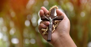 Wooden cross bead necklace holding in hands, natural blurr bokeh background, soft and selective focus. photo