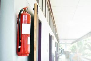 A red fire extinguisher is installed on a white cement wall in the front porch of the building to be used to extinguish a fire in the event of a building fire. photo