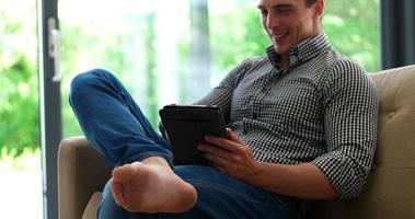 Man is Laying on Couch at Home and Using Tablet photo