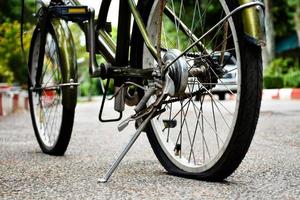 Closeup view of rear wheel of old bicycle which is flat and parked on pavement in the public park, soft and selective focus. photo