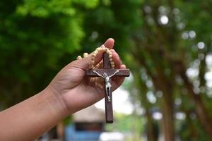 Wooden cross bead necklace holding in hands, natural blurr bokeh background, soft and selective focus. photo