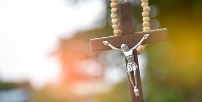 Wooden cross bead necklace hanging, natural blurr bokeh trees background, soft and selective focus.