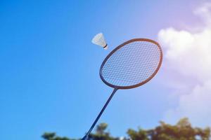 raqueta de bádminton y volante de bádminton contra un fondo nublado y azul, concepto de juego de bádminton al aire libre. enfoque selectivo en la raqueta. foto