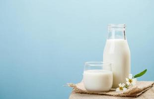 A bottle of milk and glass of milk on a wooden table on a blue background, tasty, nutritious and healthy dairy products