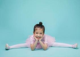 bella niña asiática sonriente con traje rosa está bailando un ballet en la escuela, espacio vacío en una foto de estudio aislada en un colorido fondo azul